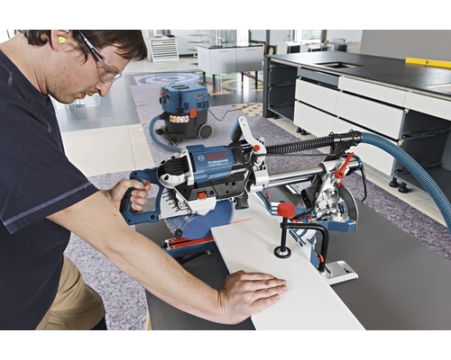 Man zaagt een werkstuk met een afkort- en verstekzaag, waarbij een stofzuiger zorgt voor netheid