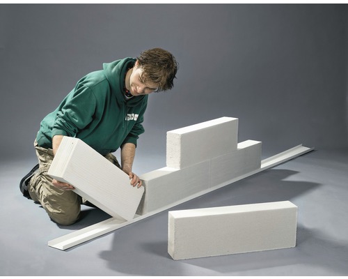 Een man bouwt een muur van cellenbetonblokken met een geleiderail.