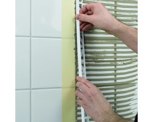 Een man bevestigt een tegelprofiel aan een wand met tegels.