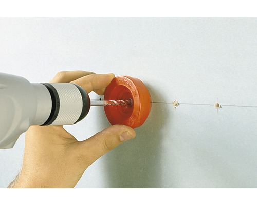 Een persoon boort met een boormachine en een stofkap in een muur.