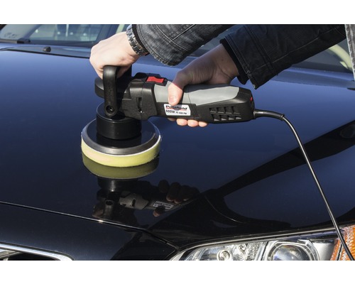 Een persoon polijst een auto met een polijstmachine.