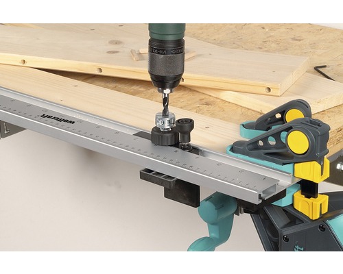 Een boormachine met deuvelboor mal boort in een houten plank met Wolfcraft deuvelklemmen.