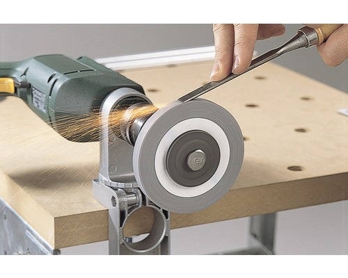 Een slijpschijf is bevestigd aan een boormachine terwijl een persoon er een steekbeitel op slijpt en er vonken ontstaan.