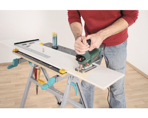 Een persoon zaagt een werkstuk met een decoupeerzaag op een werkbank.