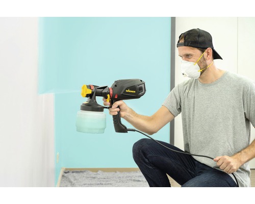 Een man gebruikt een Wagner verfspuit om een muur te schilderen.