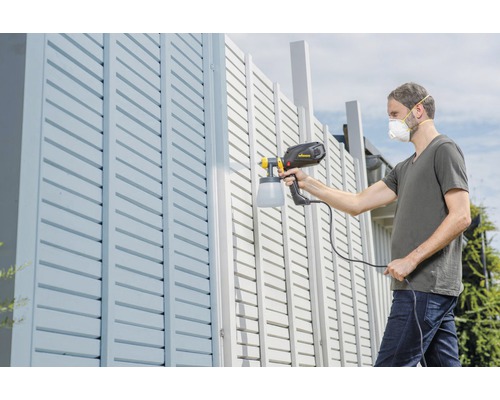 Man schildert een hek met een verfspuit.