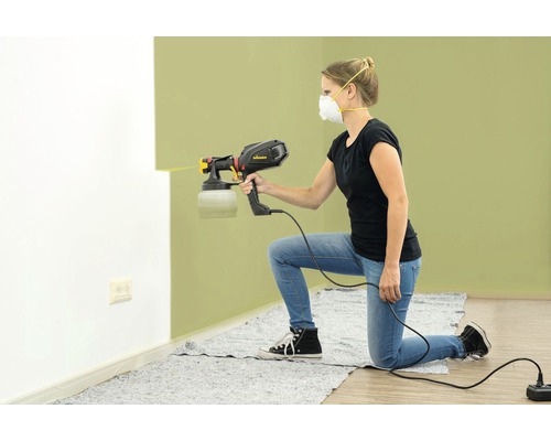 Vrouw gebruikt een verfspuit om een muur te schilderen.