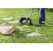 Een persoon gebruikt een grastrimmer in de tuin om gras langs een stenen pad te maaien.