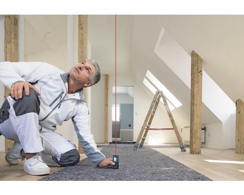 Ambachtsman gebruikt een laser afstandsmeter in een zolderkamer om nauwkeurige metingen te verrichten.