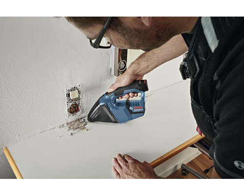 Een vakman zuigt bouwstof op een werkblad met een accustofzuiger.