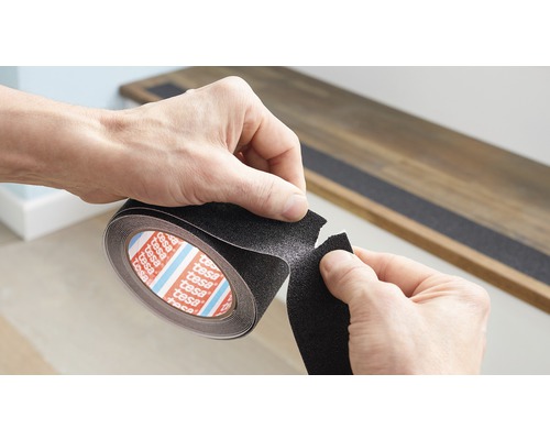 Iemand snijdt een stuk antislip tape van een Tesa-rol af om het op een trap aan te brengen.