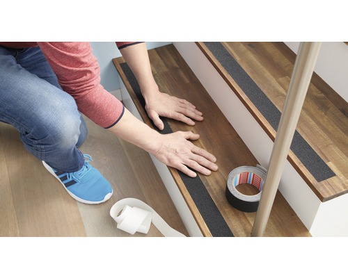 Persoon bevestigt antislipstrips op een houten trap.