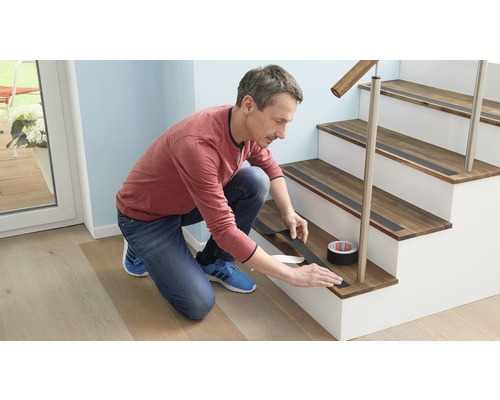 Man brengt antislipband aan op een houten trap. Rol antislipband zichtbaar.