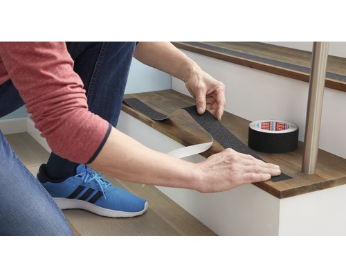 Iemand bevestigt antislip tape op een trap om de veiligheid te verhogen.