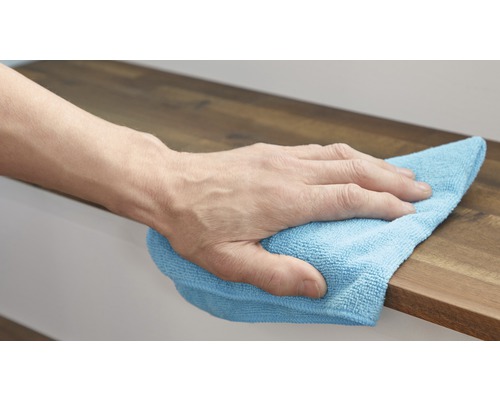 Een hand veegt met een schoonmaakdoek over een houten oppervlak.