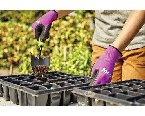 Persoon vult zaaibak met aarde en tuinschep, beschermd door tuinhandschoenen