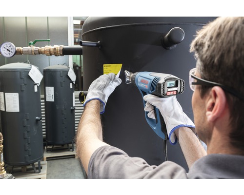 Een persoon verwijdert met een heteluchtpistool een etiket van een olietank.