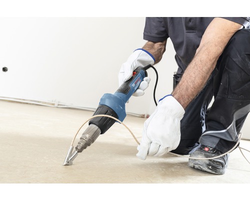 Ambachtsman bewerkt vloer met heteluchtpistool van het merk Bosch
