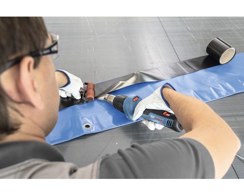 Een persoon last een folie met een heteluchtpistool en een aandrukrol.