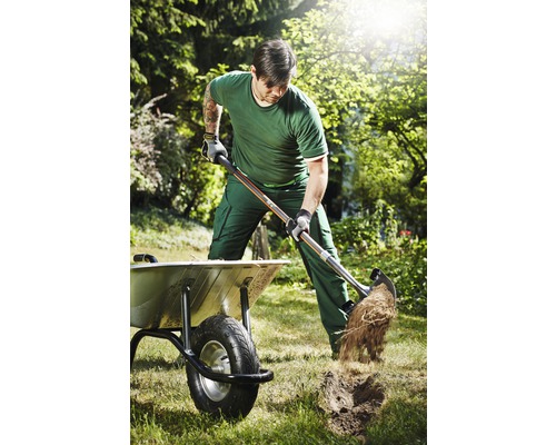 Man graaft met een spade in een tuin naast een kruiwagen.