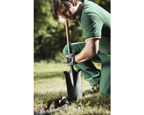 Een man knielt in de tuin en graaft een gat met een spade.