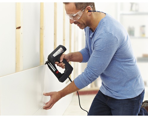 Een man bevestigt wandpanelen aan een muur met een elektrische tacker.
