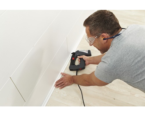 Man bevestigt een plint met een elektrische tacker aan een wandpaneel.