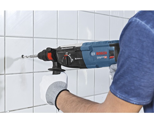 Iemand boort een gat in een betegelde muur met een boorhamer