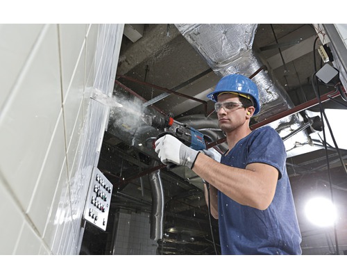 Een bouwvakker boort met een boorhamer in een muur.