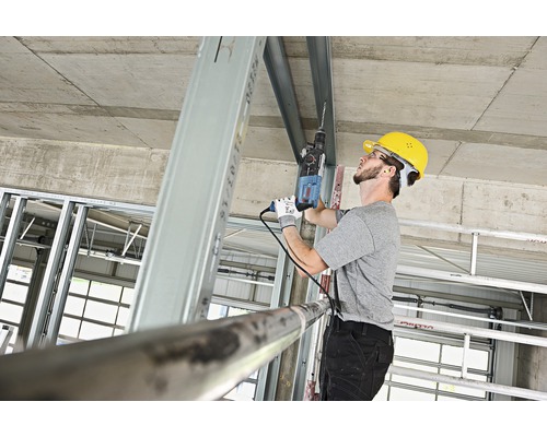 Ambachtsman boort met een boormachine in een metalen profiel op een bouwplaats.