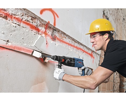Een bouwvakker boort met een boorhamer een gat in een muur.