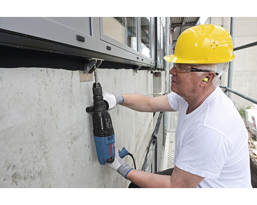 Ambachtsman boort met een boorhamer een gat in een betonnen muur
