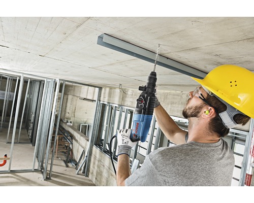 Een vakman boort met een boorhamer in een betonnen plafond op een bouwplaats.
