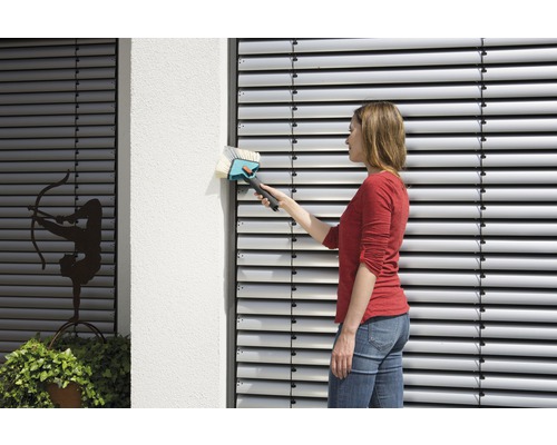 Vrouw maakt jaloezieën schoon met een jaloezieborstel op een gebouw