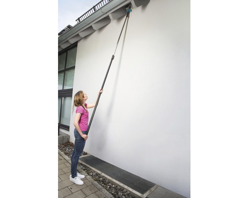 Vrouw reinigt dakgoot met telescopische steel en borstel.