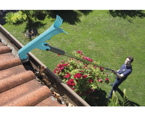 Een man maakt een dakgoot schoon met een dakgootreiniger, waarbij bladeren worden verwijderd.