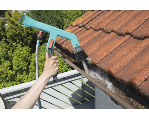 Een persoon reinigt een dakgoot met een dakgootborstel en een tuinslang.