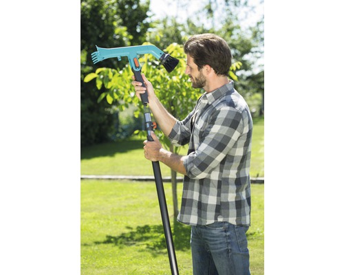 Man met een telescopische steel tuinborstel in de tuin.