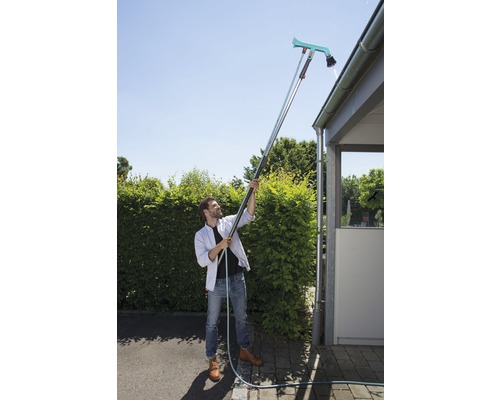 Man reinigt de dakgoot met een dakgootreiniger en telescoopsteel.