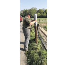 Man bevestigt een paalvoet aan een houten paal in de tuin