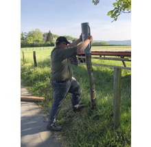 Een persoon bevestigt een paaldrager aan een hekpaal buitenshuis.