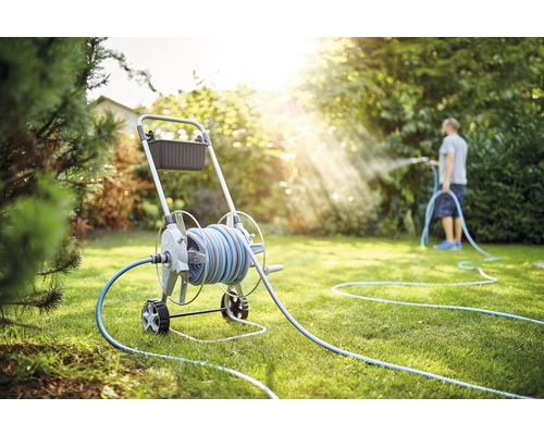 Tuinscene met slangwagen en persoon die het gazon besproeit