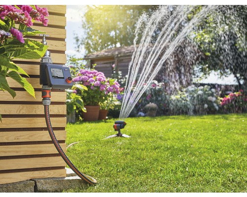 Tuinbewateringssysteem met bedieningspaneel, slang en gazonsproeier in werking