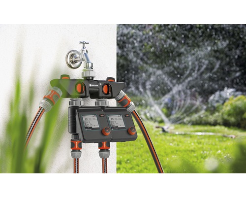 Gardena Logo. Gardena besproeiingscomputer aan een huismuur met aangesloten slangen en een gazonsproeier op de achtergrond.