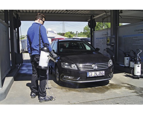 Een man maakt een auto schoon met een drukspuit in een wasstraat.