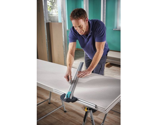 Een man snijdt een gipsplaat met een gipsplaatsnijder op een tafel.