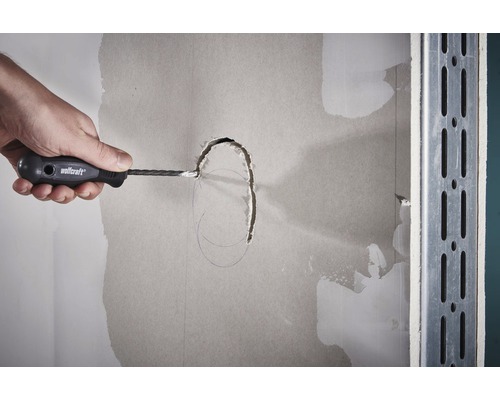 Hand snijdt met een gipsplaatsnijder een gat in een gipsplaten wand.