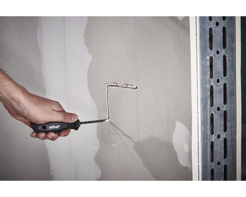 Iemand snijdt met een mes een gat in een gipsplaatwand.