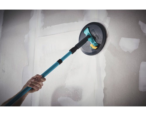 Een persoon gebruikt een plafondschuurmachine met telescopische steel op een muur.