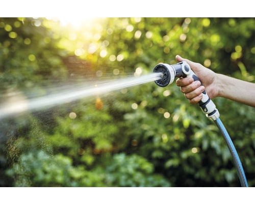 Een hand houdt een tuinslang met sproeikop vast, waar water uit spuit